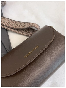Dettaglio borsa vintage in pelle marrone con tracolla geometrica e scritte dorate