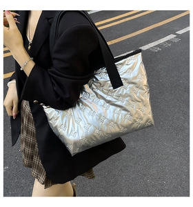 Detail of silver tote bag featuring bow-pattern quilting and a wide black shoulder strap