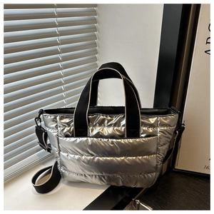 Detail of silver quilted puffer tote bag with black strap and metallic texture in soft light