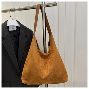 Close-up of caramel suede tote bag with wide leather strap on a minimalist hanger