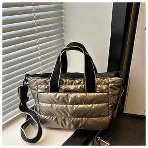 Detail of metallic bronze quilted tote bag featuring black webbing handles and wide strap