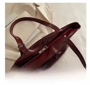 Close-up of smooth metal zipper closure on a burgundy glossy leather tote bag