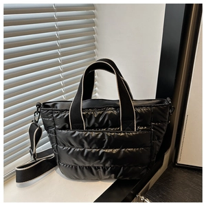 Detail of black quilted tote bag featuring glossy nylon texture and wide woven shoulder strap