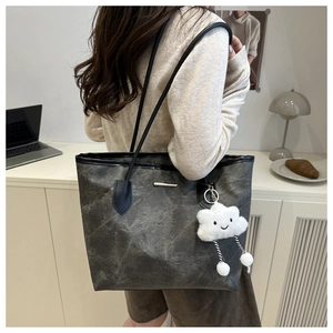Detail view of large grey tote bag with vintage texture and plush cloud charm on shoulder
