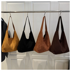 Detail of four suede tote bags in earthy tones hanging on a white door in natural light