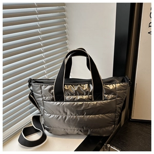 Close-up of silver quilted tote bag with padded texture and wide black woven handles