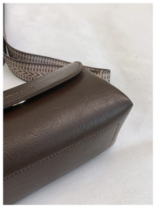 Dettaglio borsa in pelle martellata marrone con ampia tracolla geometrica e logo dorato