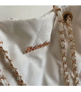 Détail rapproché du sac matelassé blanc avec chaîne dorée et logo métallique