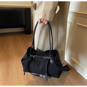 Detail of a large black suede tote bag with buckle strap on a model wearing a trench coat