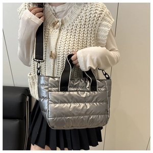 Quilted silver tote bag with black straps worn by model against a neutral background