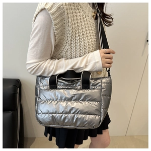 Detailed view of silver quilted tote bag with black straps worn by a female model