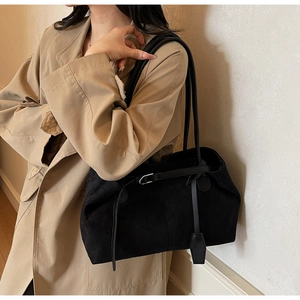 Side view of a large black matte leather tote bag styled with a khaki trench coat