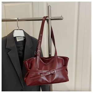 Close-up of burgundy patent leather tote bag with belt buckle detail and glossy finish