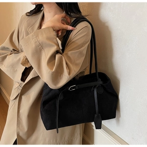 Detail of black suede tote bag with metal buckle and shoulder straps on a beige coat