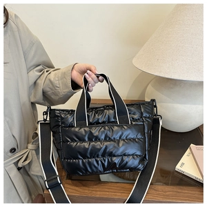 Close-up of black quilted puffer tote bag with stylish striped woven shoulder strap
