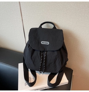 Detail of nylon backpack featuring a flap closure and woven drawstring with brand logo