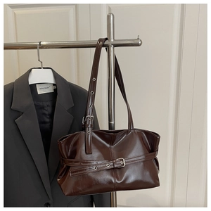 Detail view of brown glossy leather bag featuring metal eyelets and strap buckle details