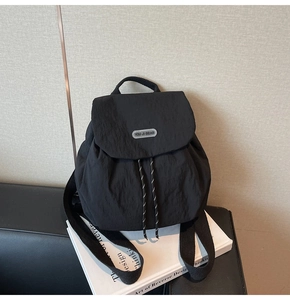 Detail of black nylon backpack with flap drawstring closure and metal logo plaque