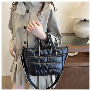 Quilted black puffer tote bag with contrast strap shown on a model in a cozy setting