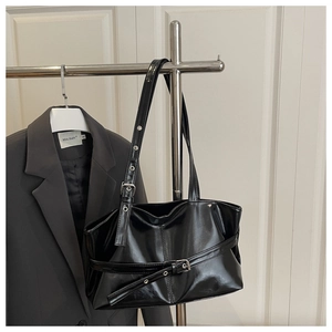 Close-up of glossy black tote bag with buckle detail hanging on a metal rack