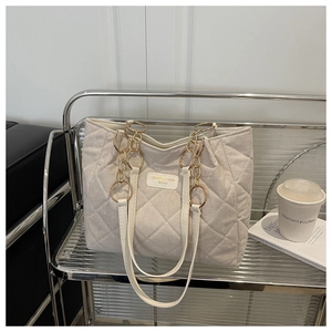 Detail of cream suede tote bag with diamond quilting and gold chain strap on display