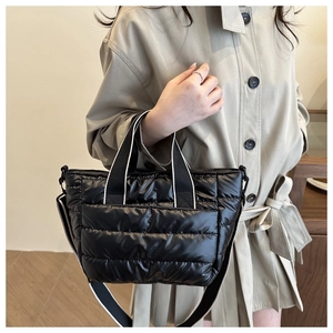 Detail of black quilted tote bag with puffer texture and striped shoulder strap