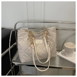 Detailaufnahme der elfenbeinfarbenen Stepptasche mit Rautenmuster und Goldkettenriemen