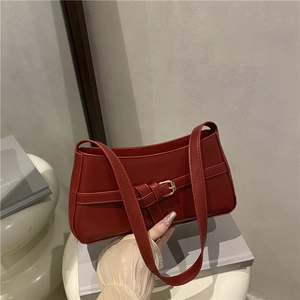 Classic red baguette shoulder bag with gold buckle detail on a minimalist white table