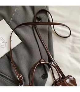 Detail of dark brown glossy pleated handbag with adjustable long shoulder strap