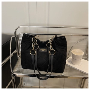 Detail of black quilted tote bag featuring golden metal rings and branded label