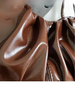 Close-up of dark brown glossy pleated leather material with fine stitching details
