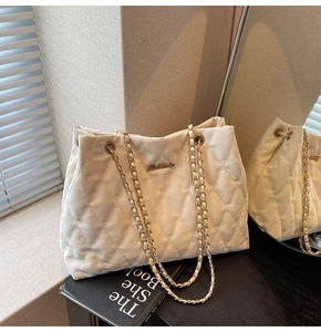 Détail d'un sac cabas beige matelassé avec bandoulière chaîne dorée et logo métallique