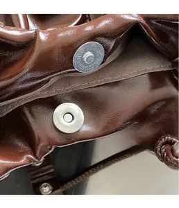 Macro shot of metallic magnetic buckle closure on a glossy brown pleated leather handbag