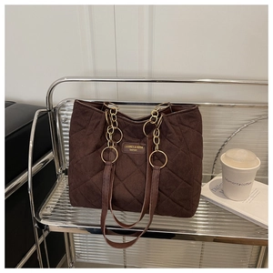 Detail of dark brown quilted tote bag with chain strap on a modern metal shelf