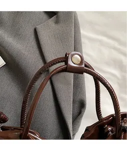 Detail of dark brown patent leather bag handle with woven texture and pearl snap button