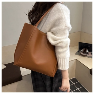 Detail of a large vintage brown leather tote bag worn by a model in a modern office setting