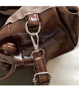Detail of adjustable strap buckle and metal hook on dark brown gathered handbag