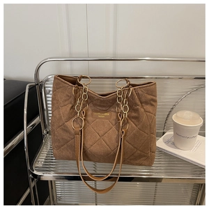 Detail of brown quilted tote bag with chain strap and leather logo patch on metal shelf