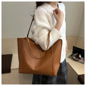 Brown leather tote bag worn by model in an office setting with laptop on the desk