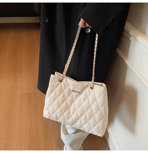 Détail d'un sac cabas beige matelassé avec bandoulière chaîne dorée et logo chic