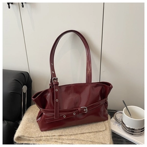 Detail of burgundy patent leather tote bag with buckle strap on a cozy beige blanket
