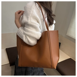 Brown large tote bag with smooth texture shown on shoulder in a cozy interior setting