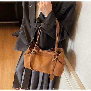 Brown suede tote bag with slim straps and metal buckle details worn by a model