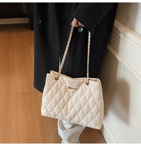 Détail d'un sac cabas en velours matelassé avec chaîne dorée et logo sur tissu ivoire