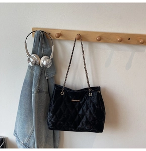 Détail d'un sac matelassé en velours noir avec bandoulière chaîne sur crochet mural