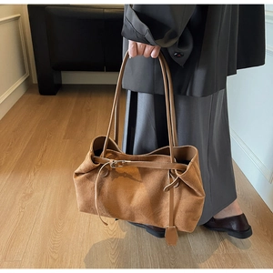 Detail of caramel suede tote bag featuring slim shoulder straps and buckle fastener