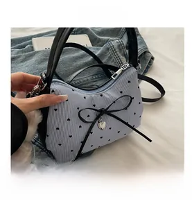 Détail du sac à main bleu rayé avec imprimé cœurs, nœud noir et pendentif cœur en métal