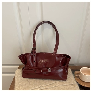 Detail of burgundy patent leather tote bag featuring buckle straps and metal eyelets