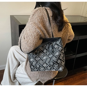 Detailed view of silver embroidery on black tote bag worn by model in casual outfit