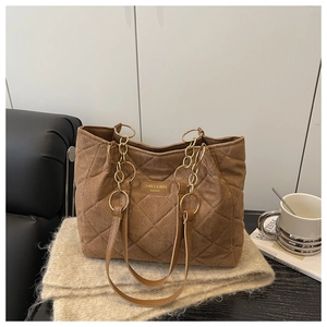Dettaglio borsa shopper trapuntata marrone con catena dorata su sfondo beige a maglia